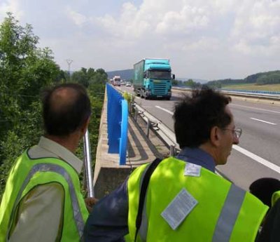 Photo of people observing trucks approaching a bridge WIM system test site in France.