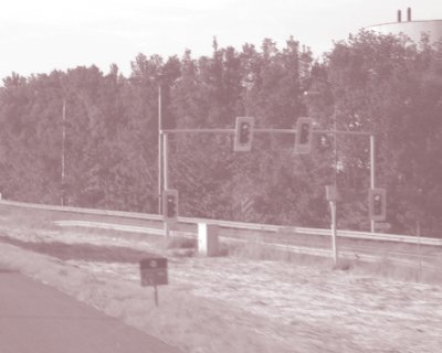 Photo of a ramp metering installation in the Netherlands, including two signal heads on an overhead gantry and two ground-mounted signal heads on each side of the ramp that face the driver at the stop bar.