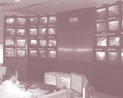 Photo of interior of Attiki Odos Traffic Management Center in Athens, Greece, with man sitting in front of computer monitors and video monitors on a wall.