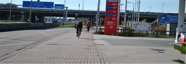 Figure 72 Current profile (from 1980s-2016) - Description: Multiple people riding in the bike lane beside a highway with a gas station to the right of them. 
