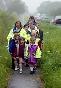 Photo of children and adults walking in a group on a path beside a roadway.