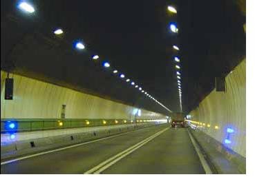 Figure looking through a tunnel with strips of lights running along each side about a quarter of the way from the bottom. All but the first lights on each side are yellow, with the first being blue. Two tracks of white lights are also shown on the ceiling.