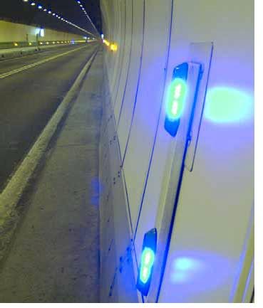 Close up photo of the blue lights on one side of the tunnel. The yellow lights on both sides, as well as the white lights on the ceiling can be seeing in the distance.