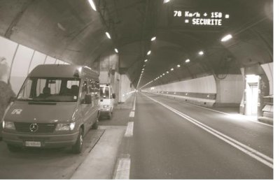 Two vehicles are shown pulled over to the far right side inside the tunnel, one behind the other. They're parked across from the refuge room which is lit with a sign.